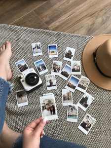 woman looking at a pile pf photos with a hat and camera by her feet
